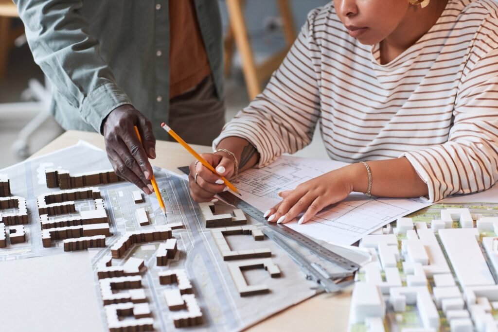 Close-up of designers working over model of building in team, they drawing blueprint and discussing mockup